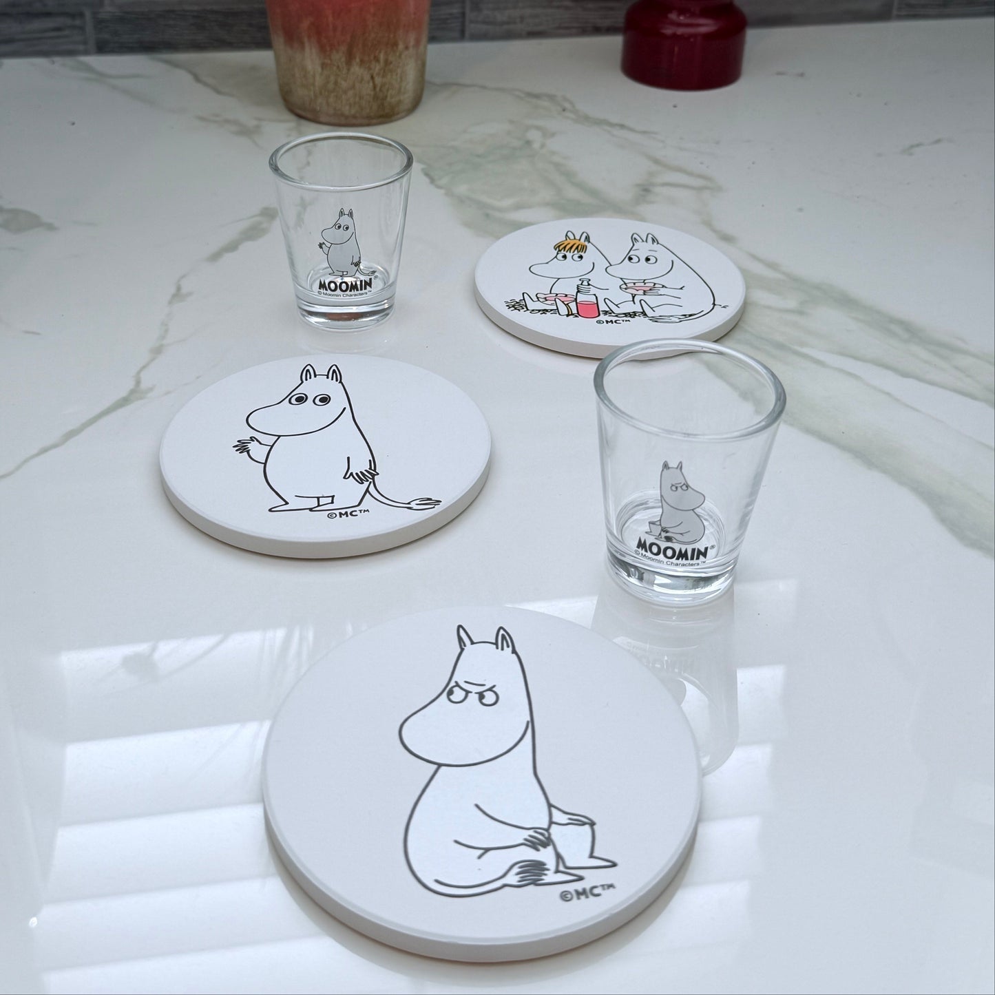 Set of coasters and glasses with Moomin character design on a marble surface
