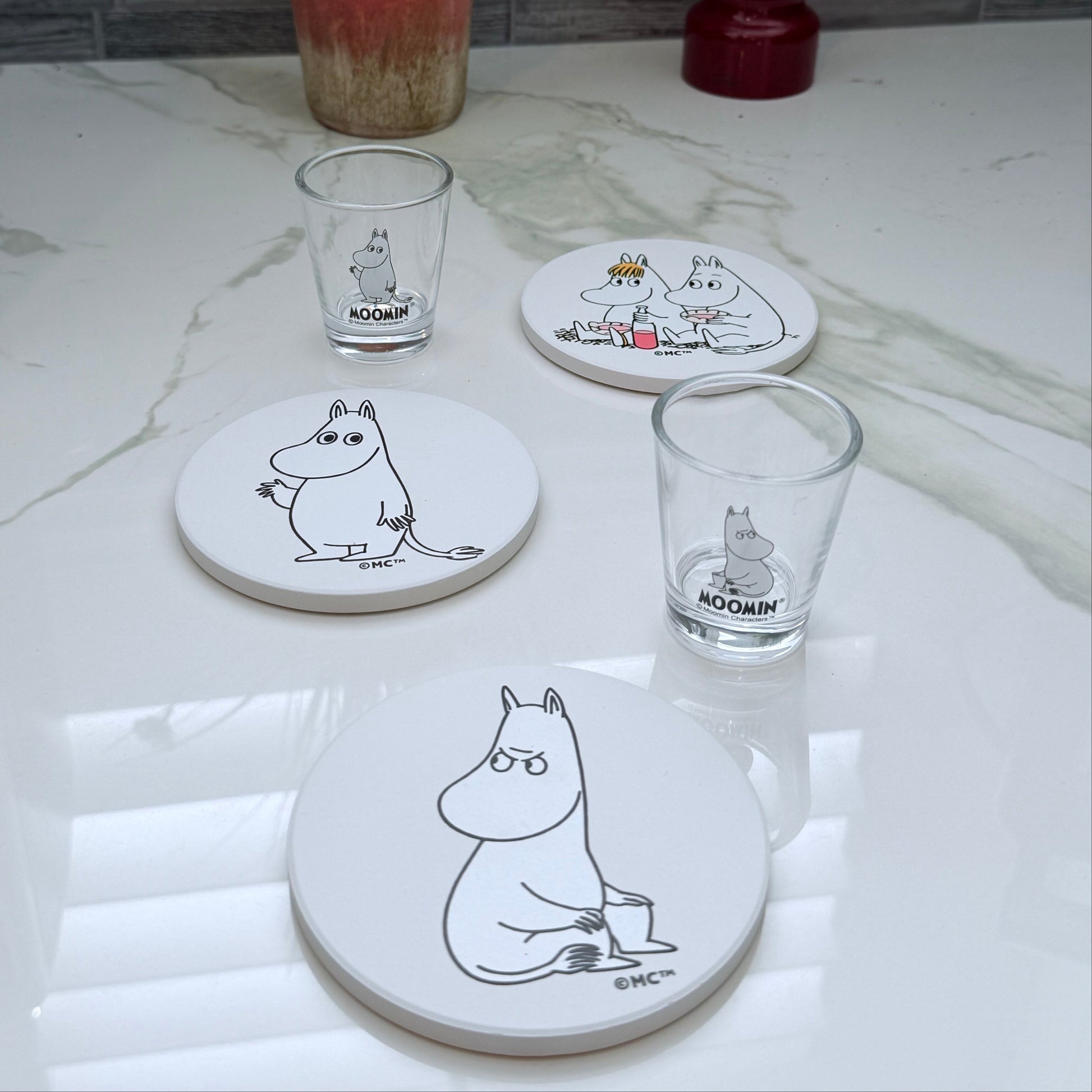 Set of coasters and glasses with Moomin character design on a marble surface