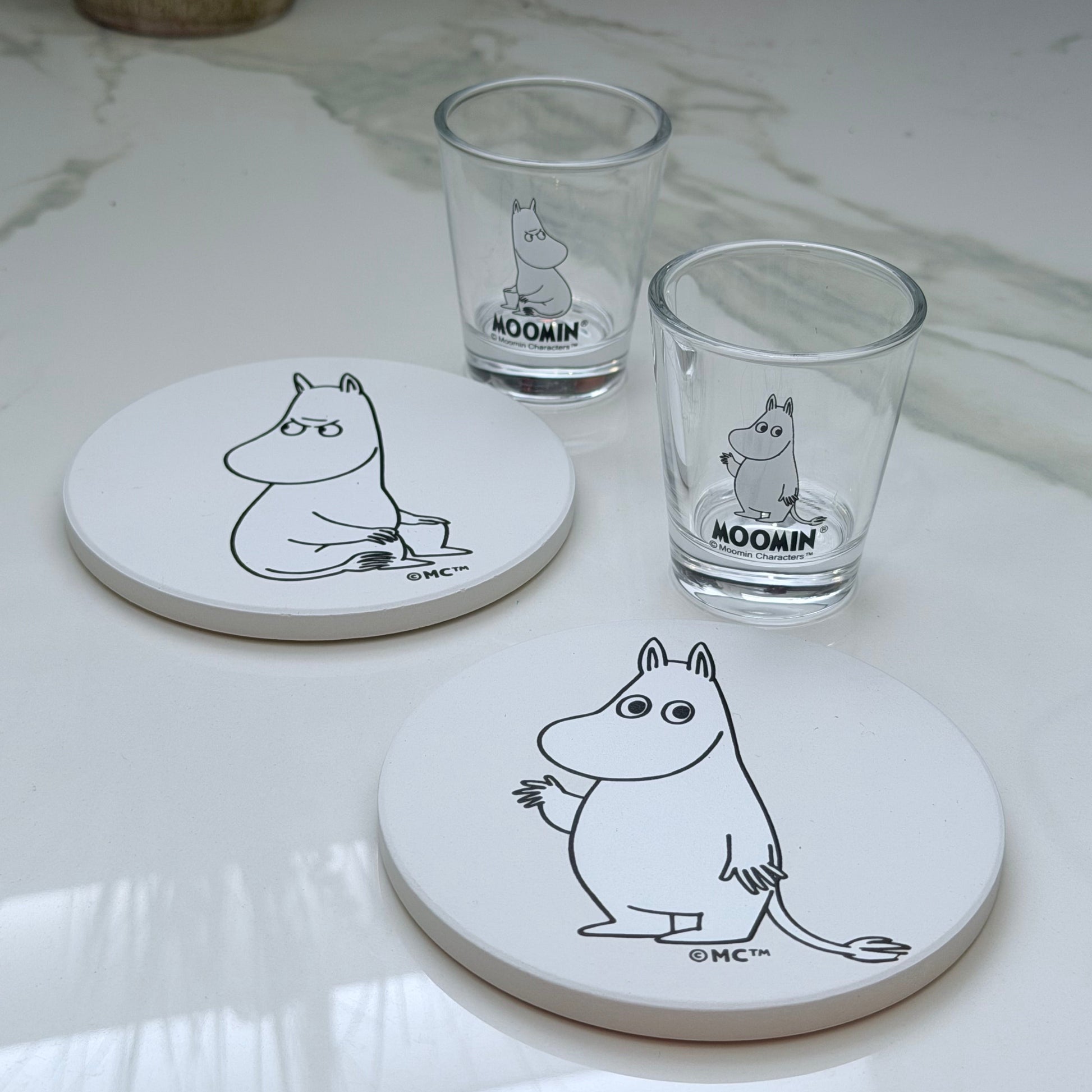 Set of coasters and glasses with Moomin characters on a white surface.